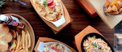 A table with various dishes including a baked dish with tomatoes, a salad, fries, and a rice dish with meat.