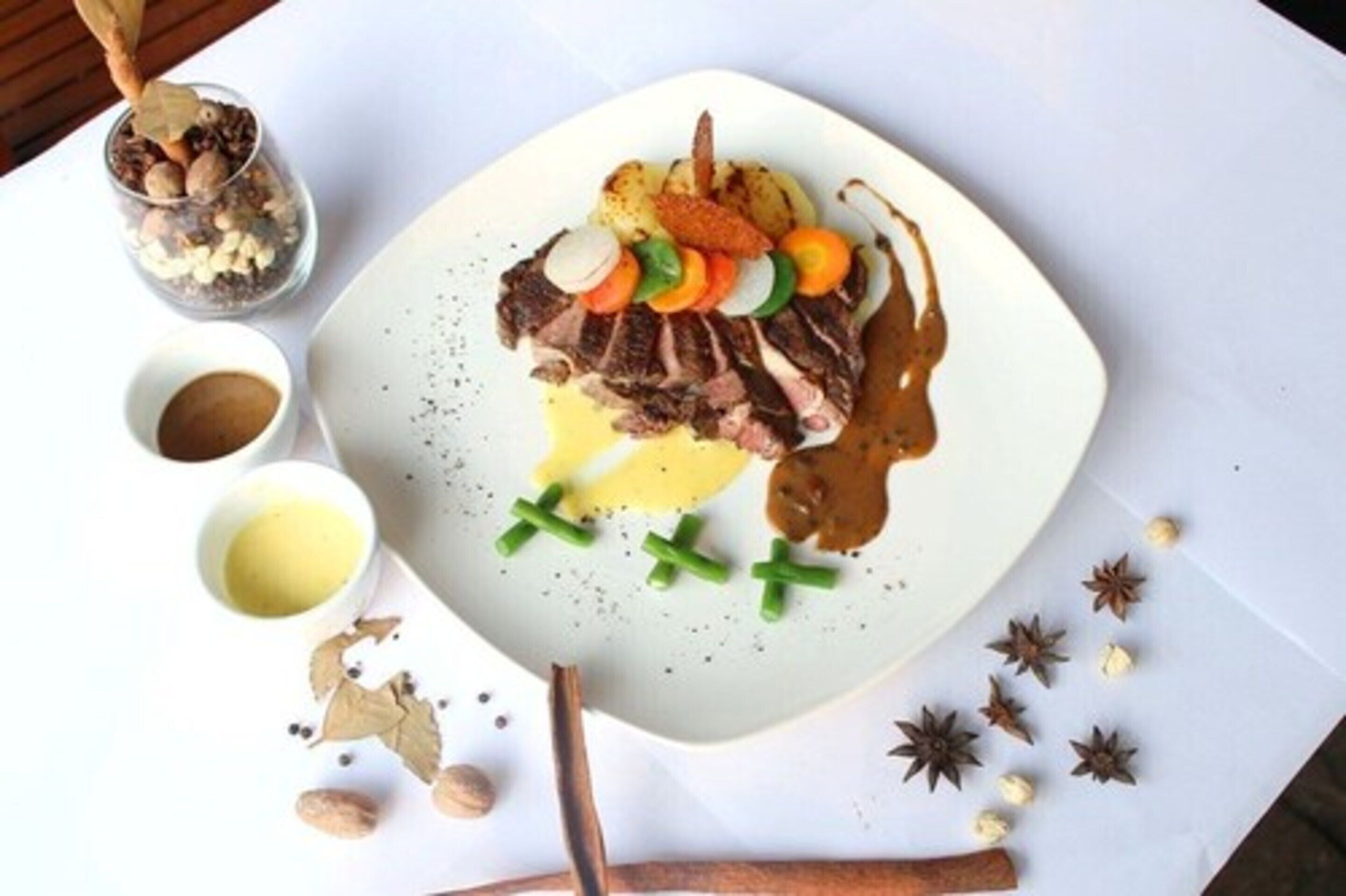 Un plato de comida con una variedad de verduras y salsa, acompañado de recipientes pequeños con salsas adicionales.