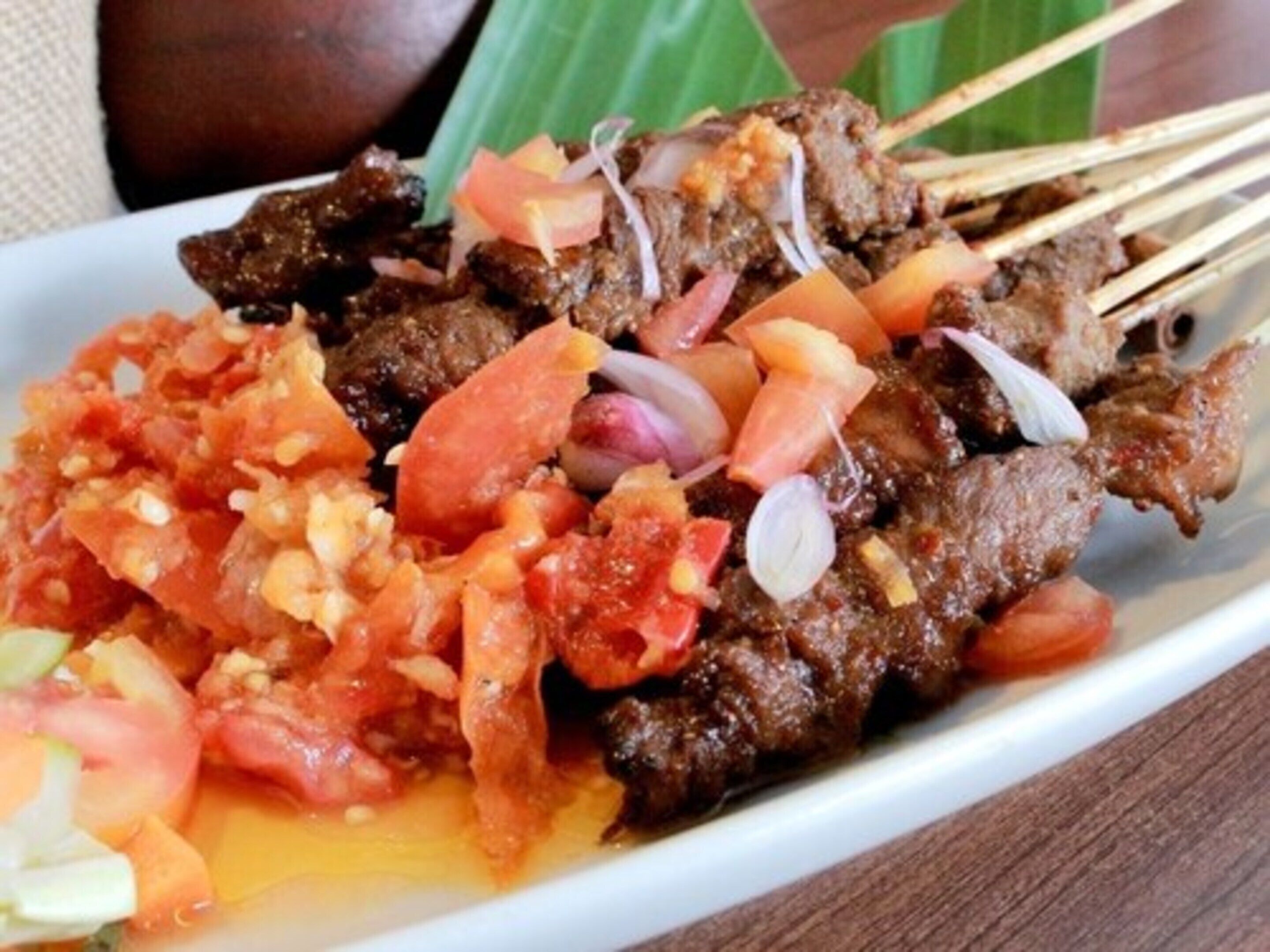 Un plato de carne ensartada acompañado de tomate y cebolla picados.
