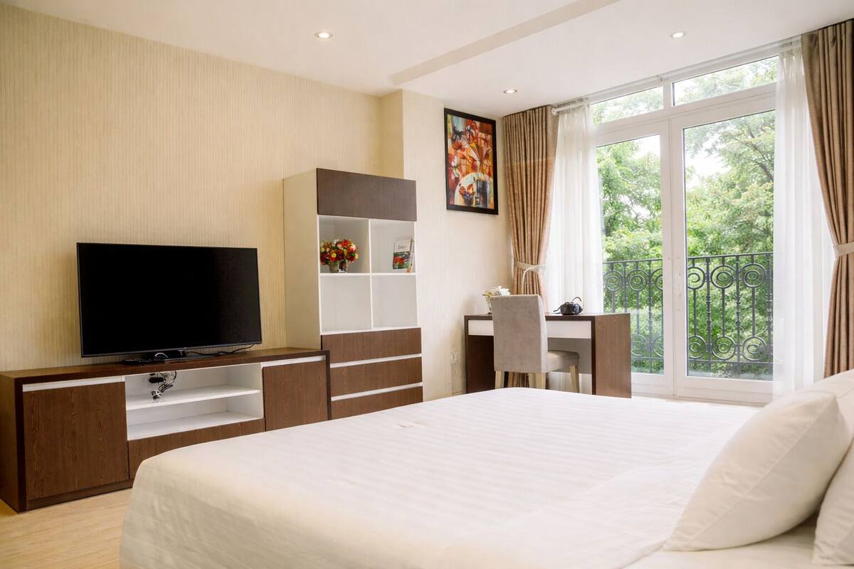 Habitación de hotel con una cama grande, televisión, escritorio con silla y ventana con vistas a zonas verdes.