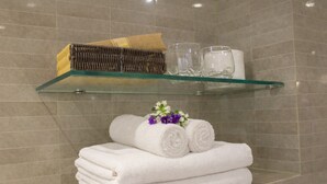 Un baño con una repisa de vidrio que sostiene toallas, un tapete de baño y artículos de aseo.