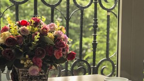 Una mesa con una taza y platillo blancos, un libro y un jarrón de flores.