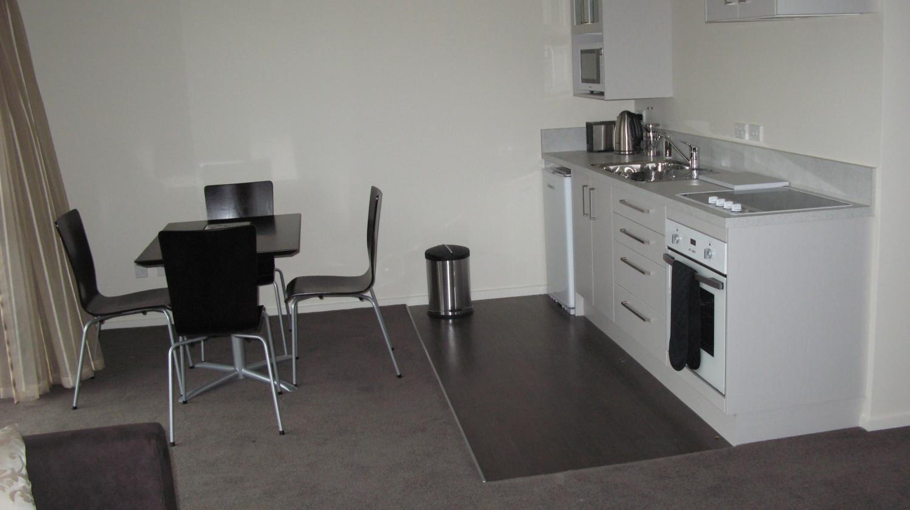 Una cocina compacta con comedor, que incluye una mesa, sillas, un cubo de basura y un horno empotrado.