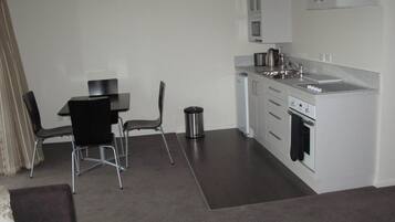 Une cuisine compacte avec un coin repas comprenant une table, des chaises, une poubelle et un four encastré.