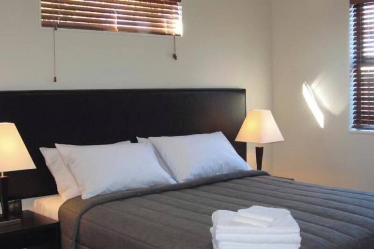 A hotel room with a bed, two bedside lamps, a window with blinds, and a folded towel on the bed.