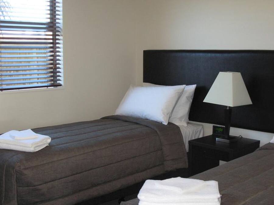 Een hotelkamer met twee bedden, een nachtkastje met een lamp en een raam met jaloezieën.