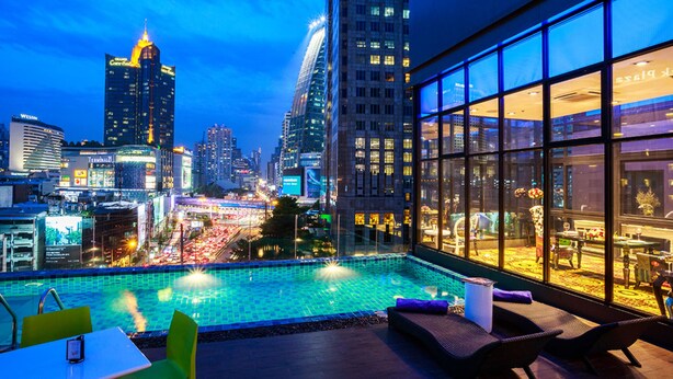 A rooftop pool with a city view, lounge chairs, and a glass wall overlooking the urban landscape. - Hotel Clover Asoke (Bangkok)