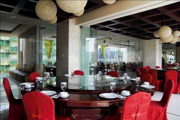 Un comedor con mesas redondas, sillas tapizadas rojas y un separador de vidrio.