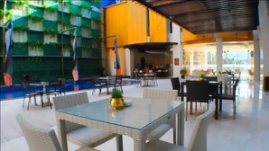 A spacious outdoor dining area with wicker furniture and a glass table, surrounded by a pool and a covered seating area. - Horison Lampung (Bandar Lampung)