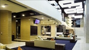 A modern hotel lobby with a curved seating area, a TV screen, and a staircase leading to an upper level. - Horison Lampung (Bandar Lampung)