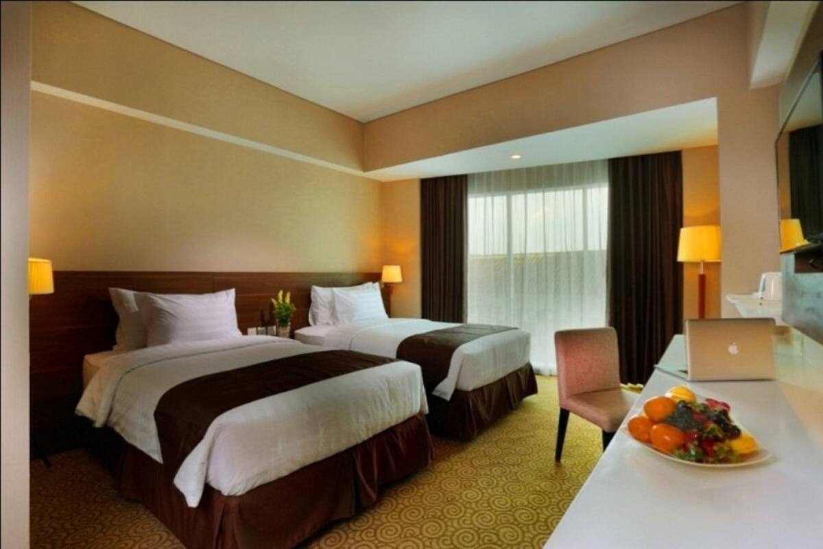 A hotel room with two beds, a desk with a laptop, and a fruit plate.