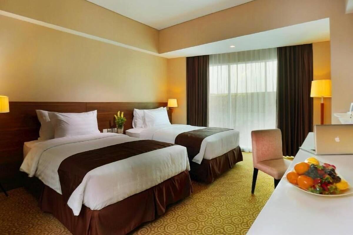 A hotel room with two beds, a desk with a laptop, and a fruit plate.