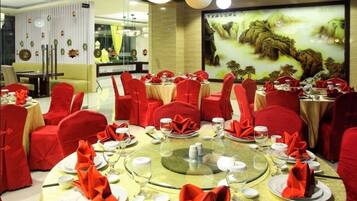 A dining area with round tables set for multiple guests, red chairs, and a large wall mural.