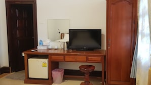 Une chambre avec un bureau en bois, une télévision, un petit réfrigérateur et une poubelle.