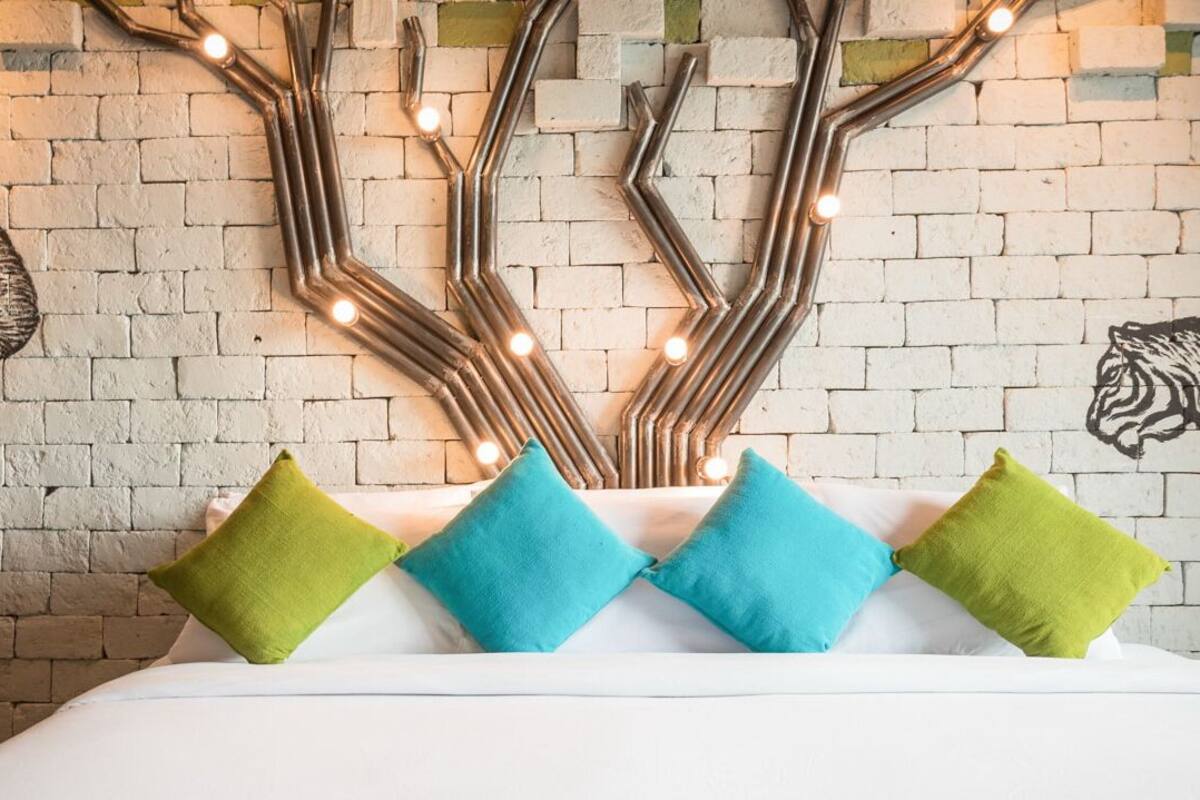 A bed with colorful pillows and a wall with a brick pattern and a tree-like light fixture.