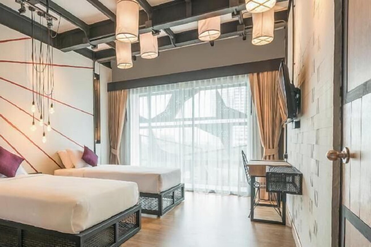A hotel room with two beds, a dining table, and a large window with curtains.