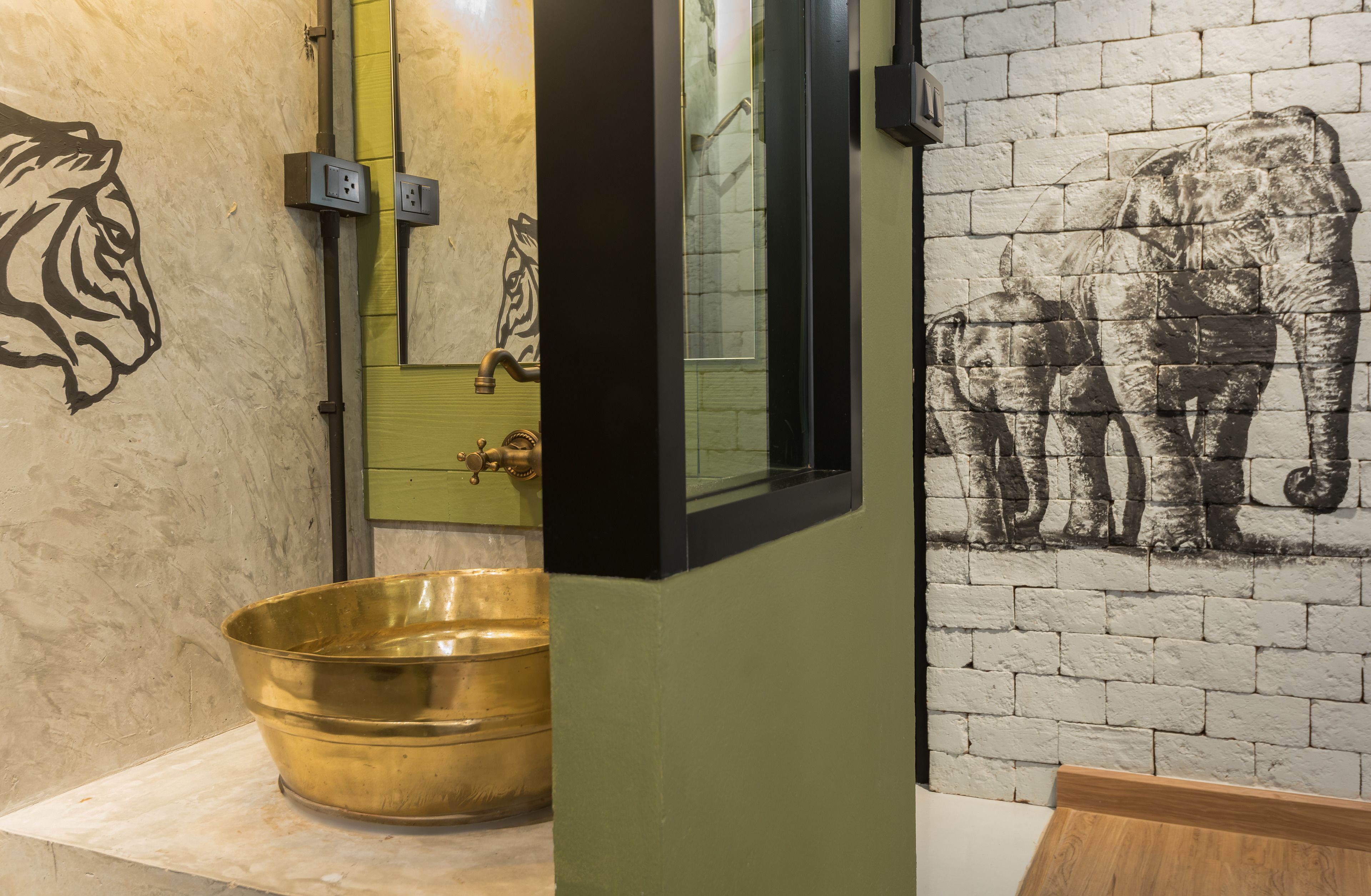 A bathroom with a large brass basin, a tiger mural, and an elephant mural on the wall.