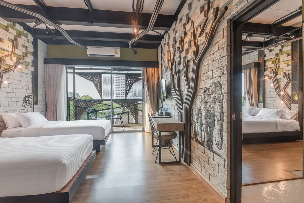 A hotel room with two beds, a desk, a balcony with a view, and a brick wall with a unique design.