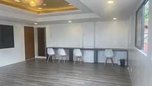 A spacious room with a wooden floor, white walls, and a ceiling with recessed lighting. There are four white chairs aligned against the wall, and a window on the right side. - Cozy Coron Inn (Coron)