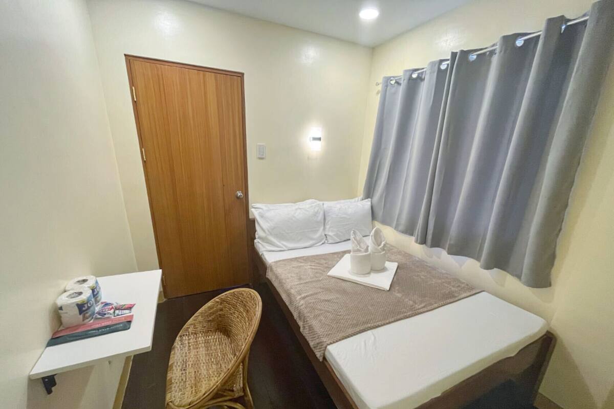 Un dormitorio pequeño y ordenado con una cama individual, una mesita de noche, una silla y una puerta.