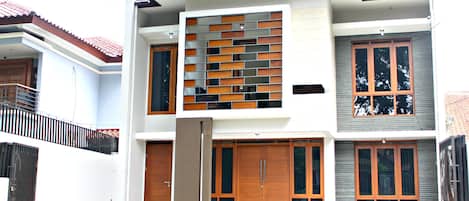 Una casa de dos pisos con diseño moderno, que cuenta con puertas de madera grandes y un balcón.