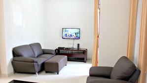 Una sala moderna con un sofá seccional, un sillón individual, un televisor de pantalla plana montado en la pared y un mueble de entretenimiento de madera oscura.