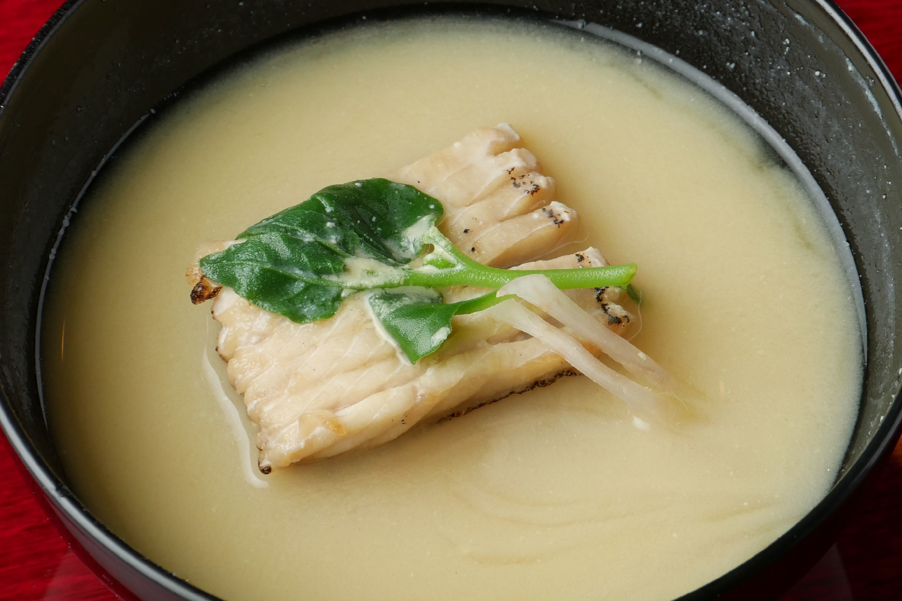 A bowl of soup with fish and greens.