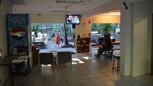 A room with a television mounted on the wall, a ceiling fan, and a view of the outside. - Frogshollow Backpackers (Darwin)