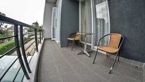 A balcony with two wicker chairs, a glass table, and a view of a residential area. - De Orion Setiabudi Villa (Bandung)