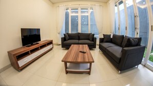 A modern living room with a wooden coffee table, a TV on a wooden stand, and two dark sofas. - De Orion Setiabudi Villa (Bandung)