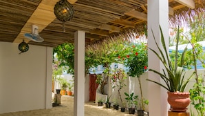 A covered outdoor area with a sandy floor, potted plants, and a wooden ceiling structure. - Masfalhi View Inn (Felidhoo)