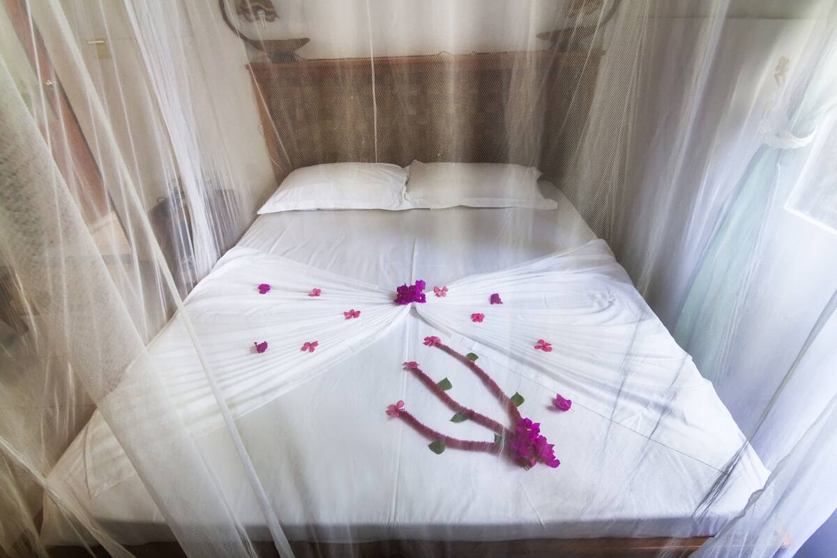 A bed with white linens and a canopy, adorned with purple flowers.