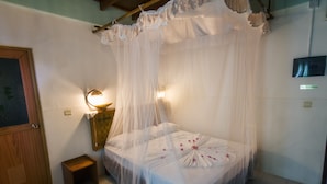 A neatly arranged bedroom with a canopy bed, a bedside lamp, a small wooden nightstand, and a 'No Smoking' sign on the wall. - Masfalhi View Inn (Felidhoo)
