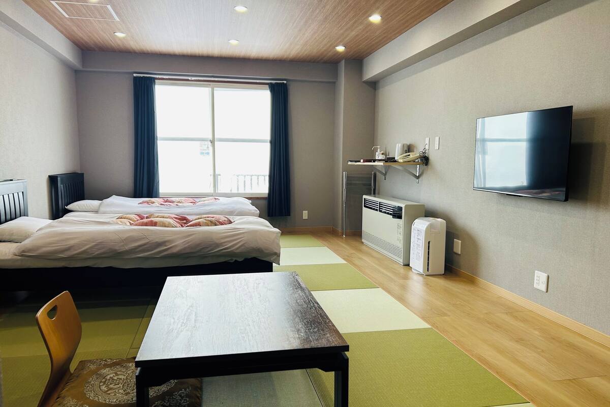 A hotel room with two beds, a TV, a heater, and a window with curtains.