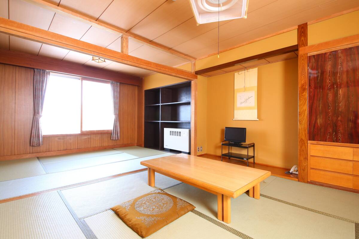 A traditional Japanese room with tatami flooring, a low wooden table, a television, and a wardrobe.