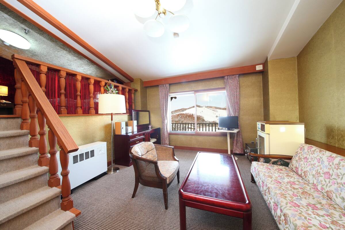A living room with a staircase, a sofa, a table, and a television.