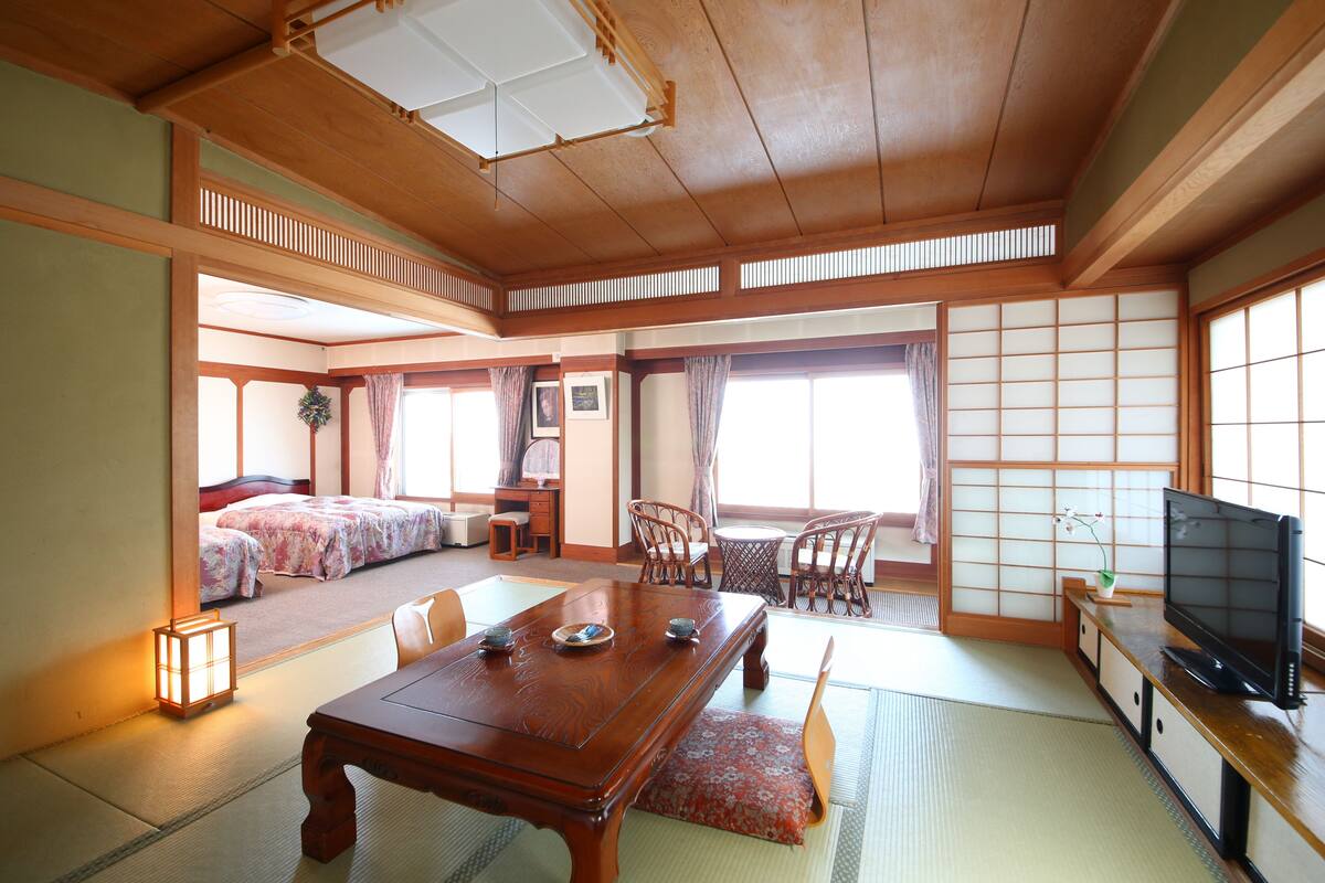 A traditional Japanese room with tatami flooring, a low wooden table, and a television on a cabinet.