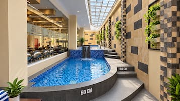 Una piscina interior con escalones que la bordean, rodeada de paredes con diseño de tablero de ajedrez y plantas en macetas.