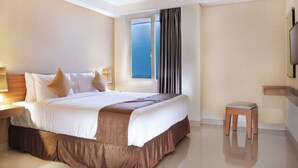 A hotel room with a large bed, a nightstand with a lamp, a small wooden stool, and a television on the wall.