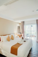 A hotel room with a large bed, a desk with a chair, and a view of the outdoors through a sliding glass door.
