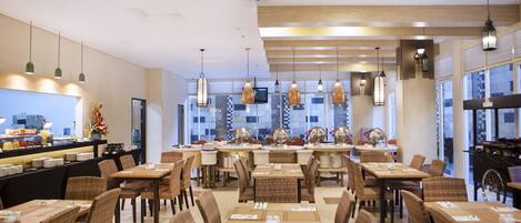 A modern restaurant with multiple dining tables and chairs, a bar area, and a television screen.