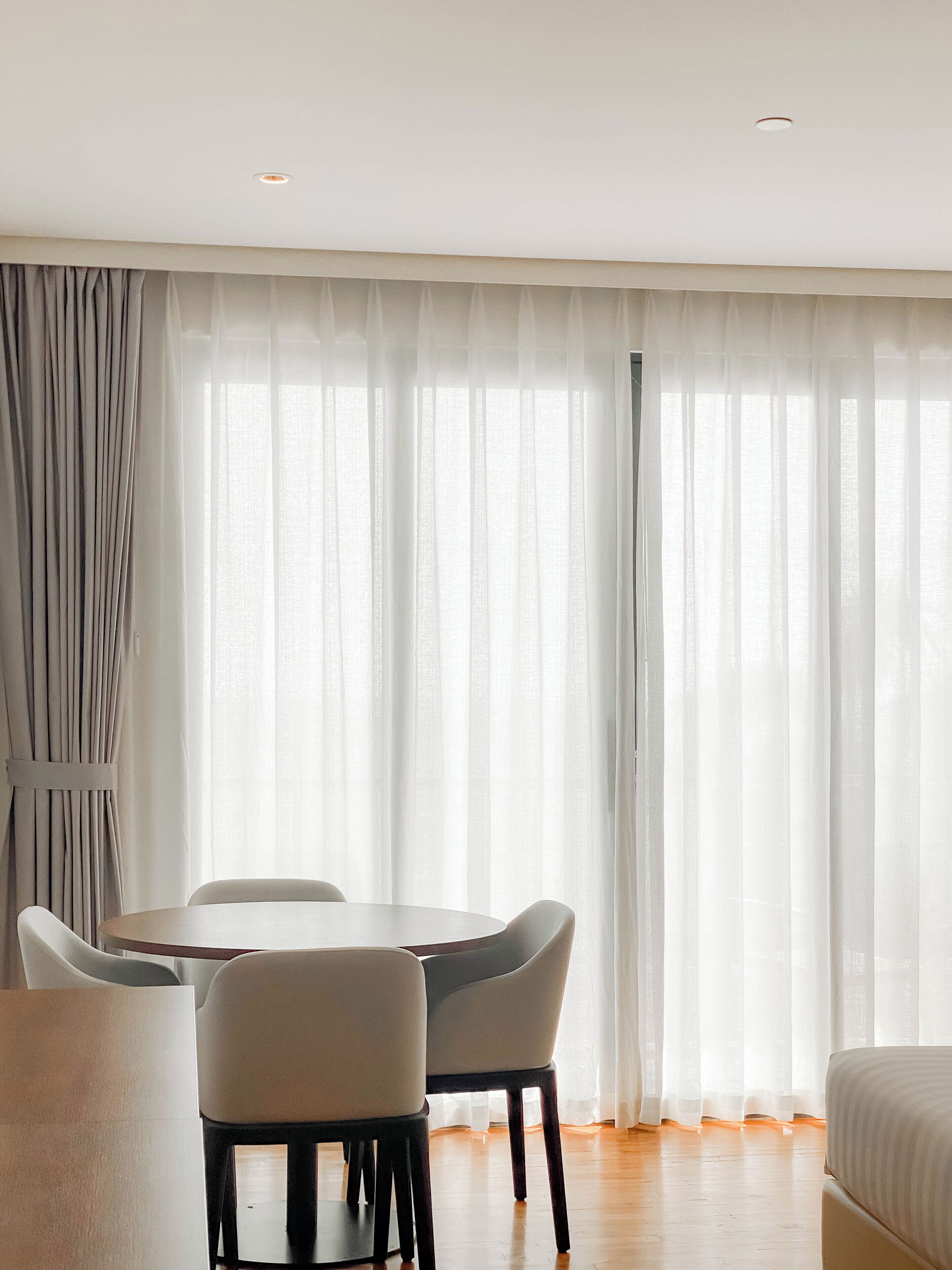 A hotel room with a dining area, a bed, and sheer curtains.