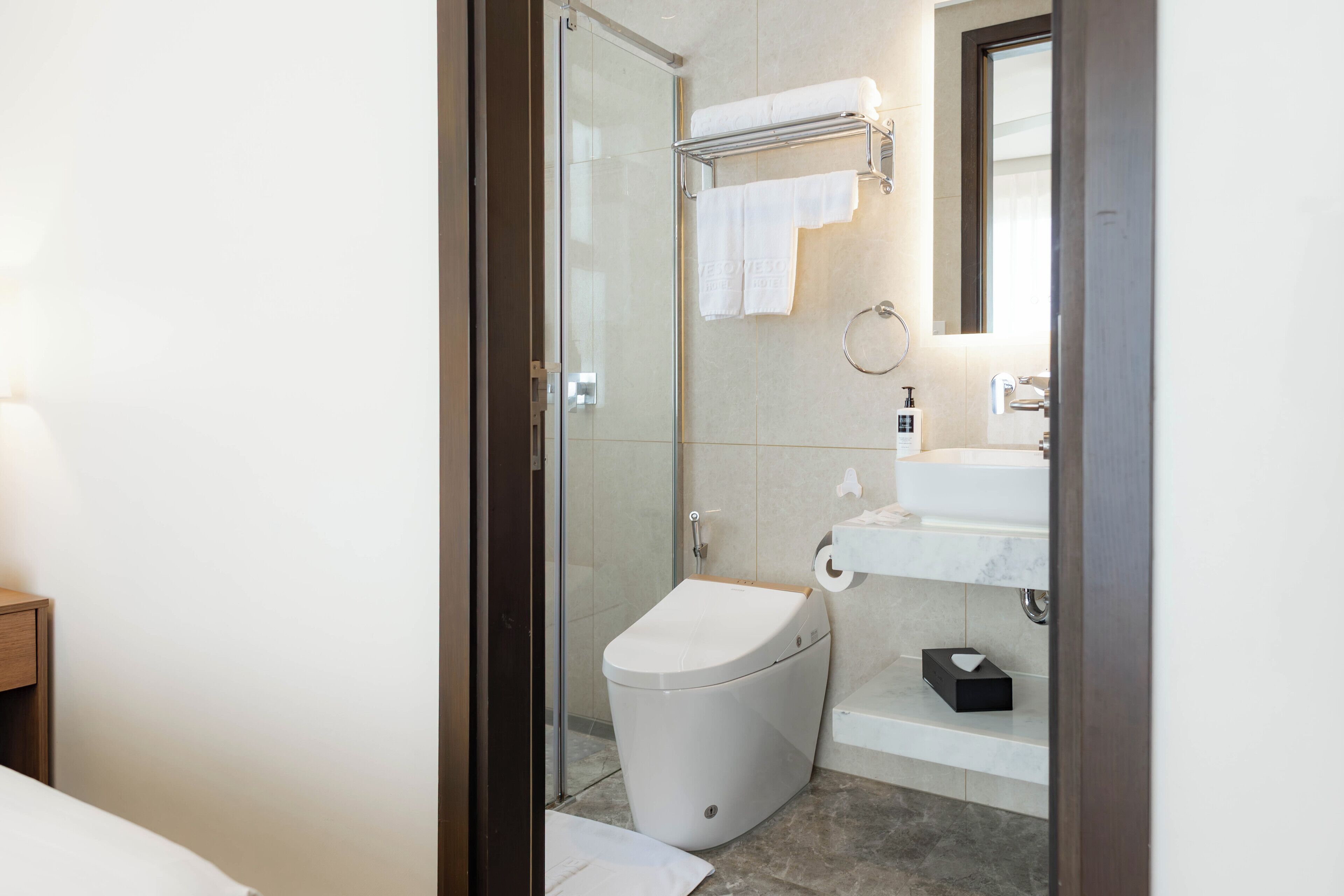 A modern bathroom with a glass-enclosed shower, a toilet, a sink with a marble countertop, and a mirror.