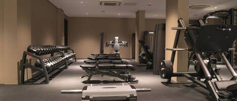 Ein Fitnessstudio mit verschiedenen Trainingsgeräten, darunter Kurzhanteln, Bänke und Kraftgeräte.