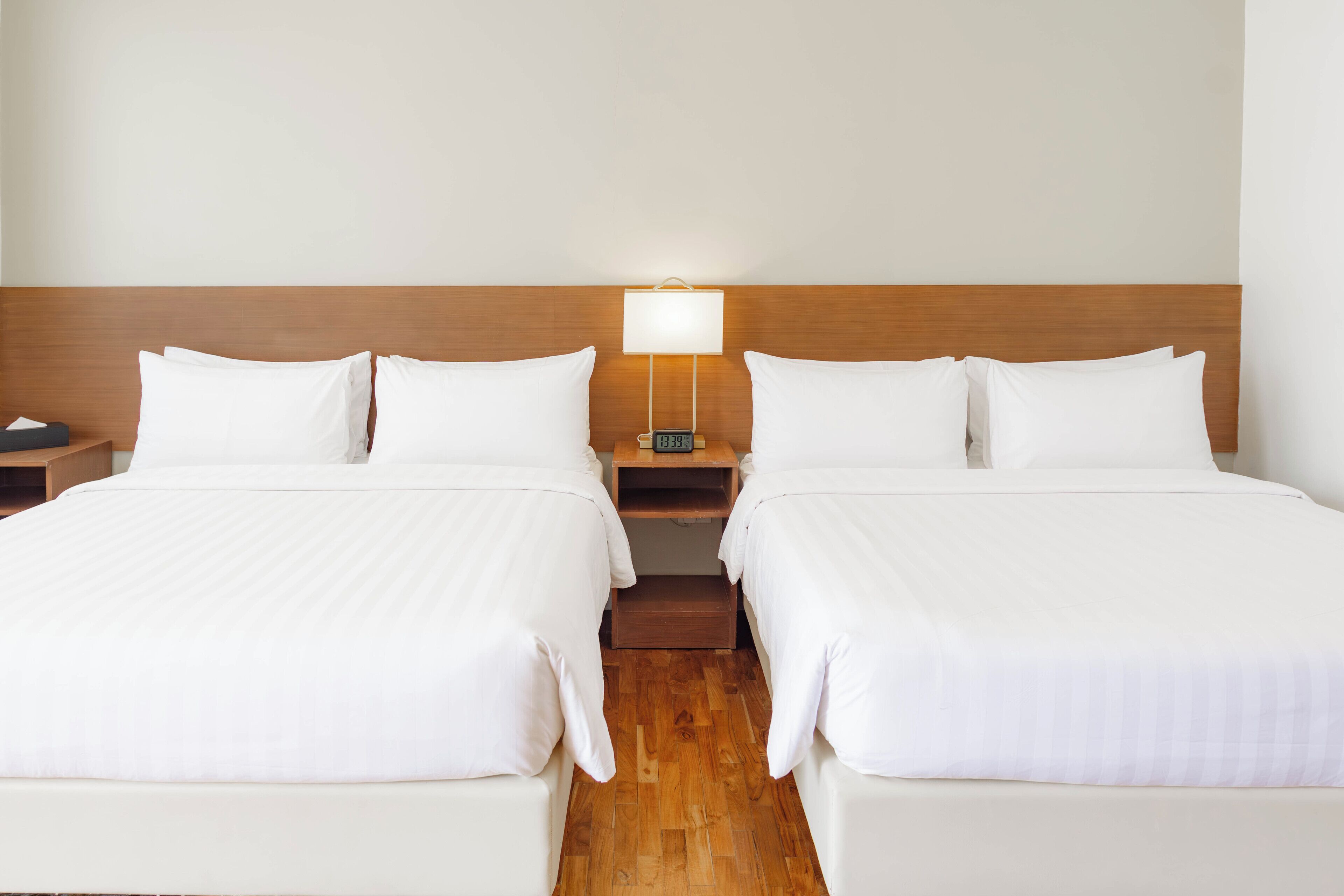 Una camera d'albergo con due letti, un comodino con una lampada e una testiera in legno.