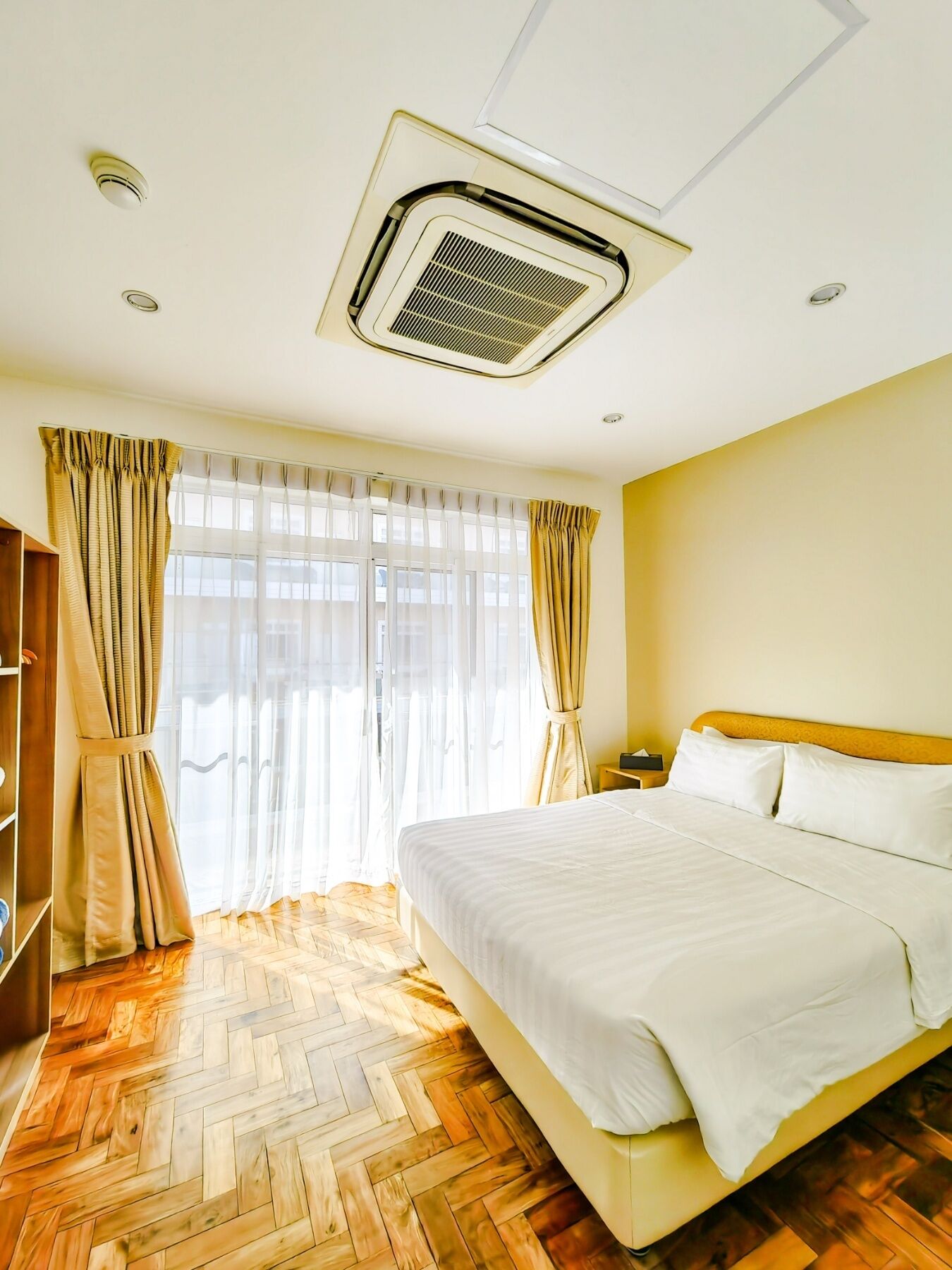 Een hotelkamer met een groot bed, houten vloeren, een airconditioner in het plafond en gordijnen.