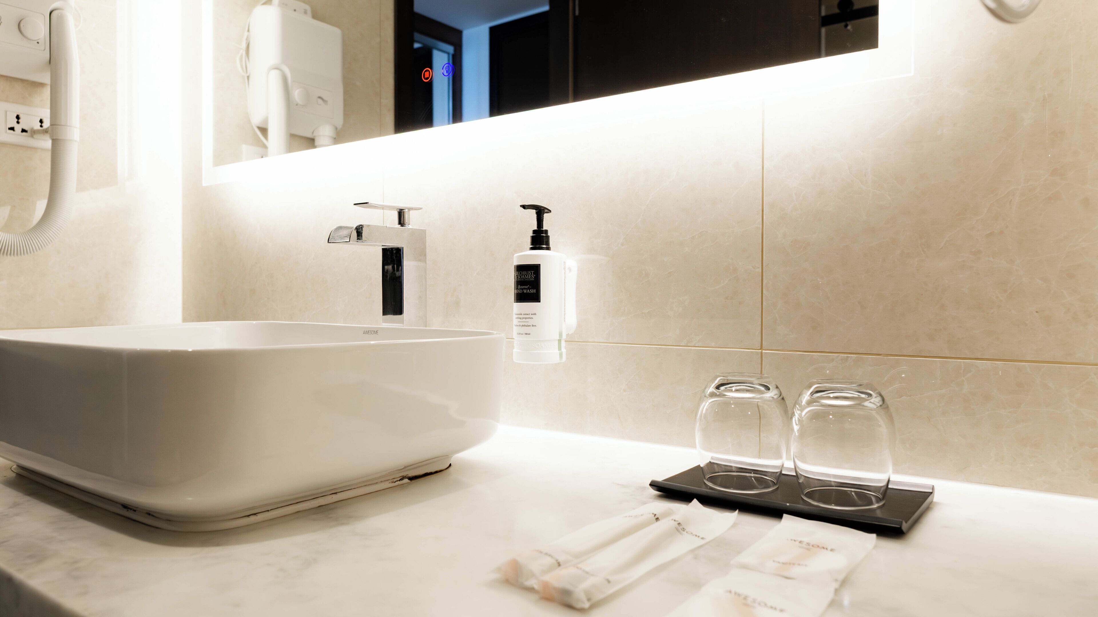 A bathroom with a white sink, a hand soap dispenser, and two empty glass containers on a tray.