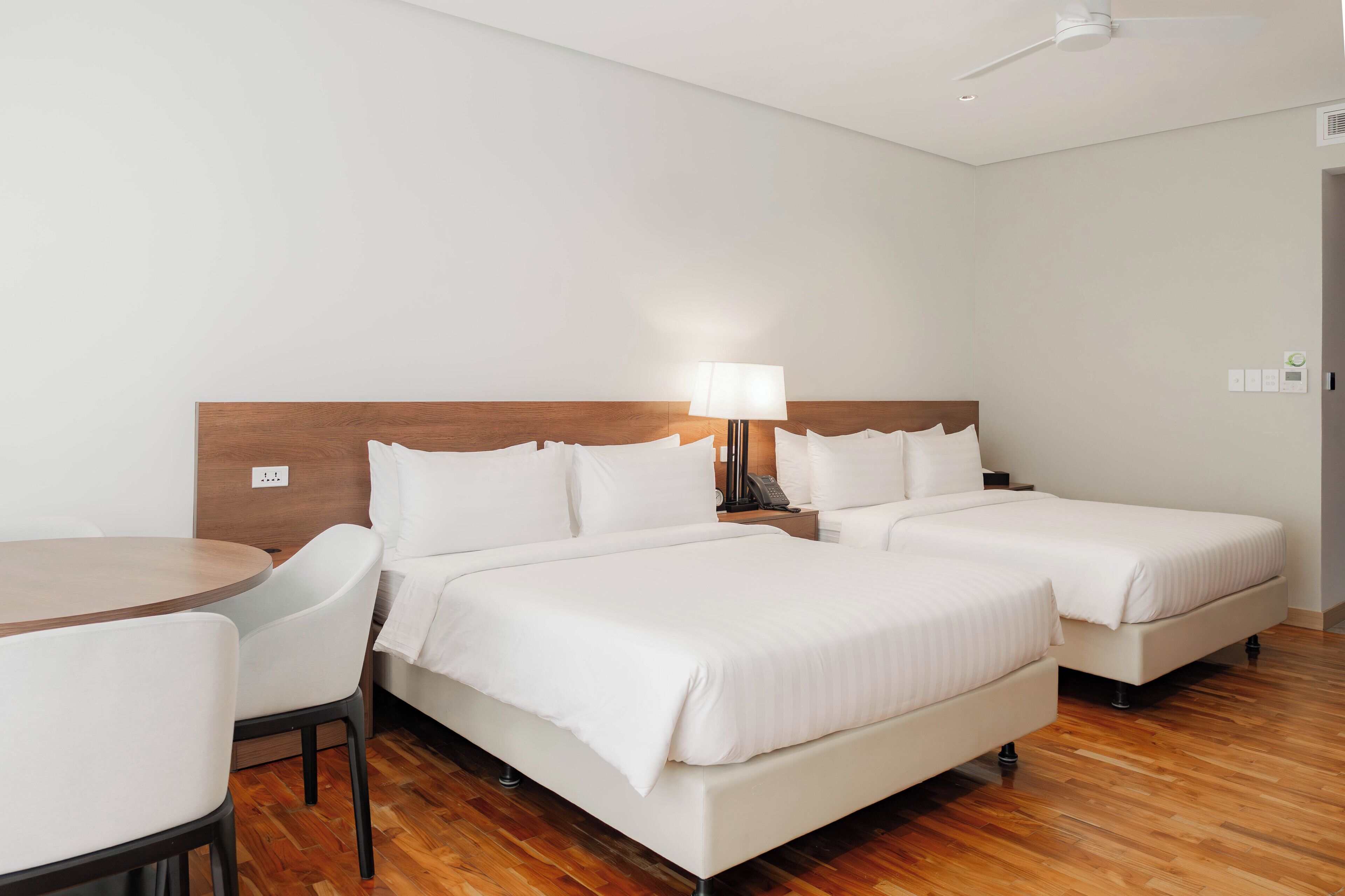 A hotel room with two beds, a round table, and a chair.