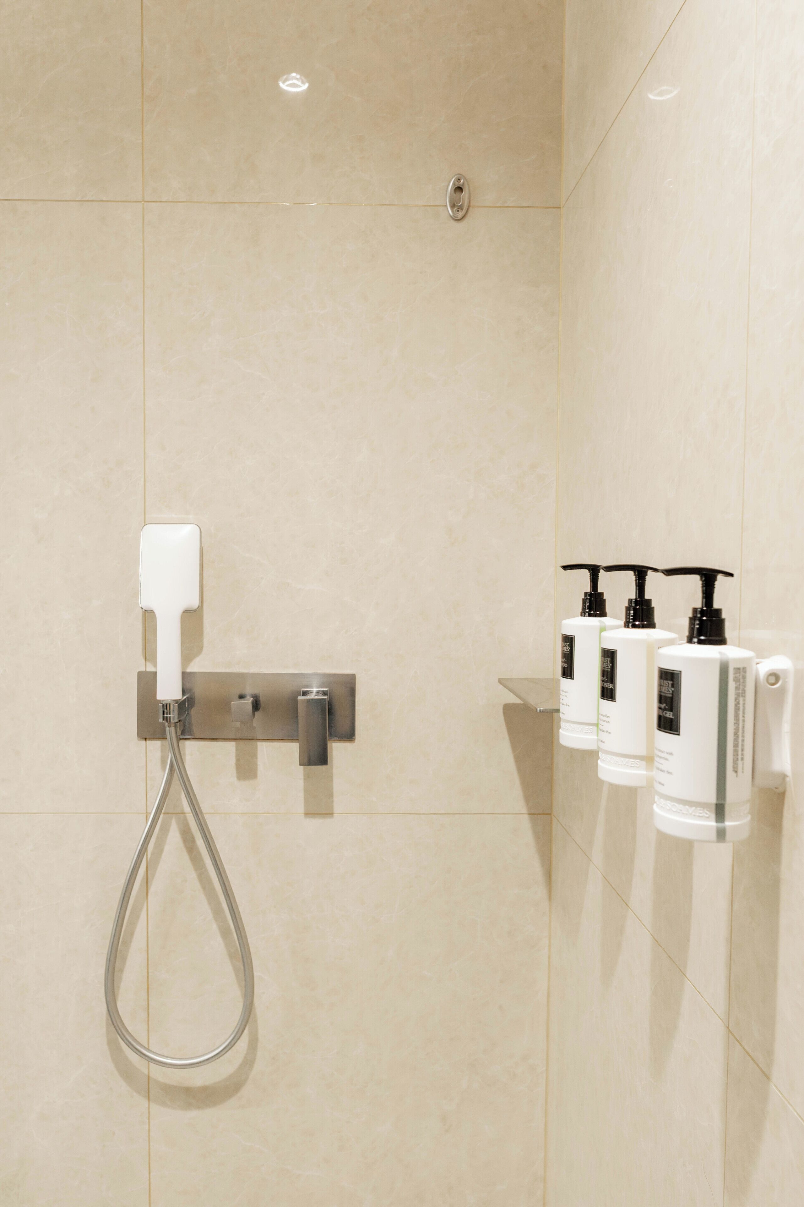 A bathroom with a shower, a hand dryer, and toiletries on a wall-mounted shelf.