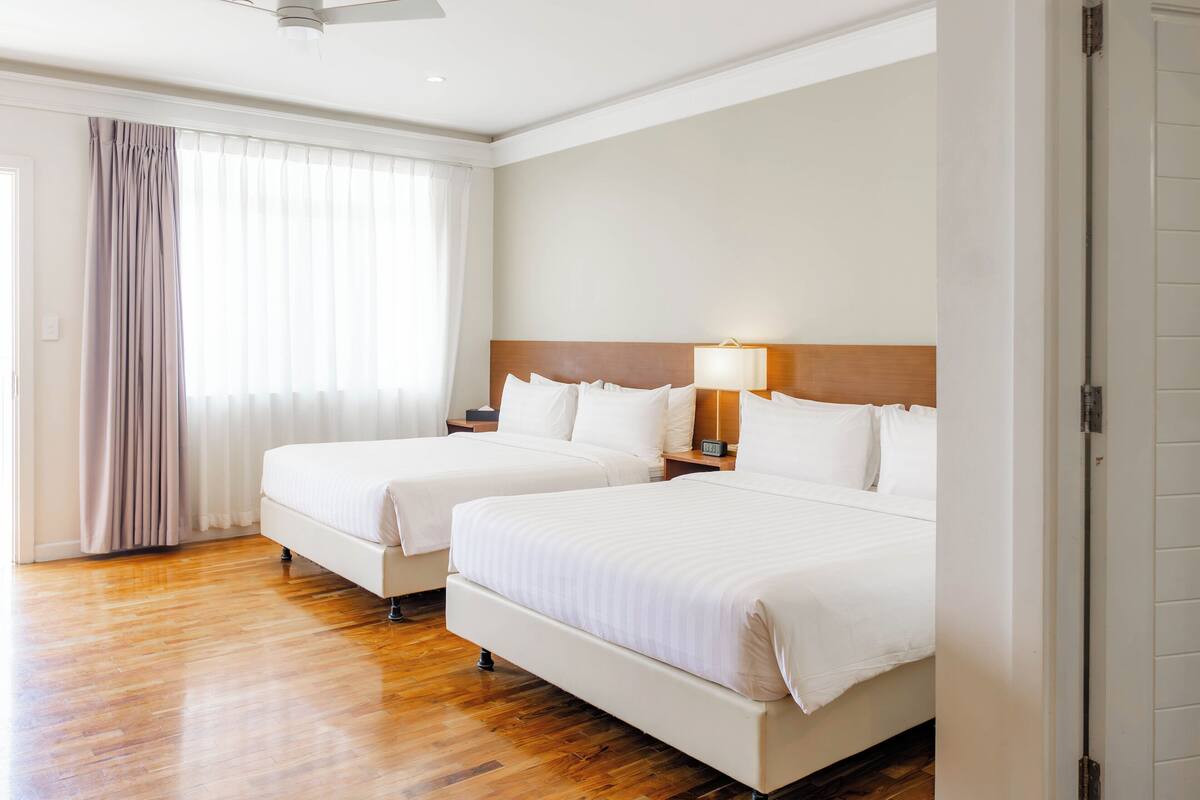 Une chambre d’hôtel avec deux lits, un plancher en bois, un ventilateur de plafond et une fenêtre avec des rideaux.